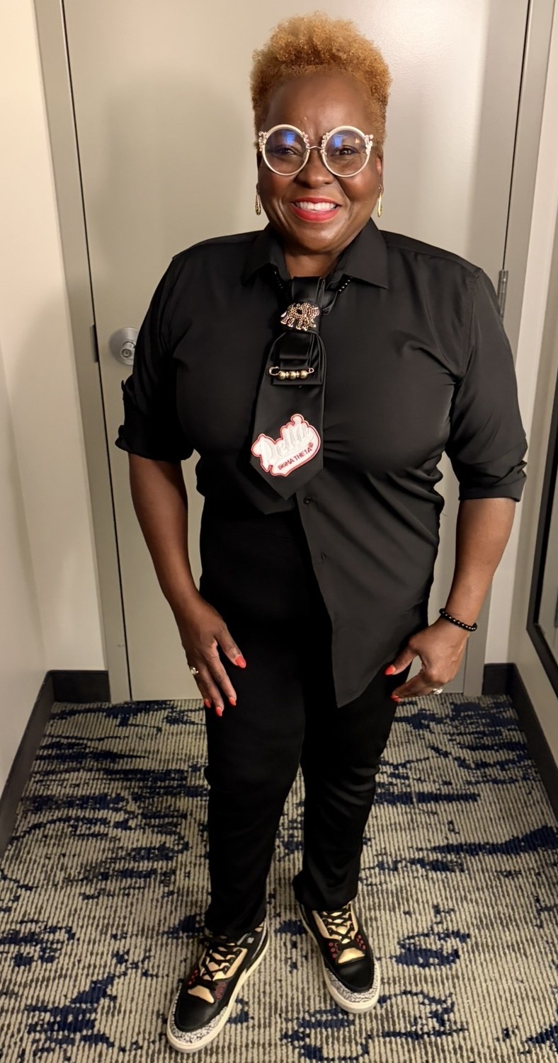 DeeDee Johnson smiling in a black button-up with a Delta Sigma Theta tie