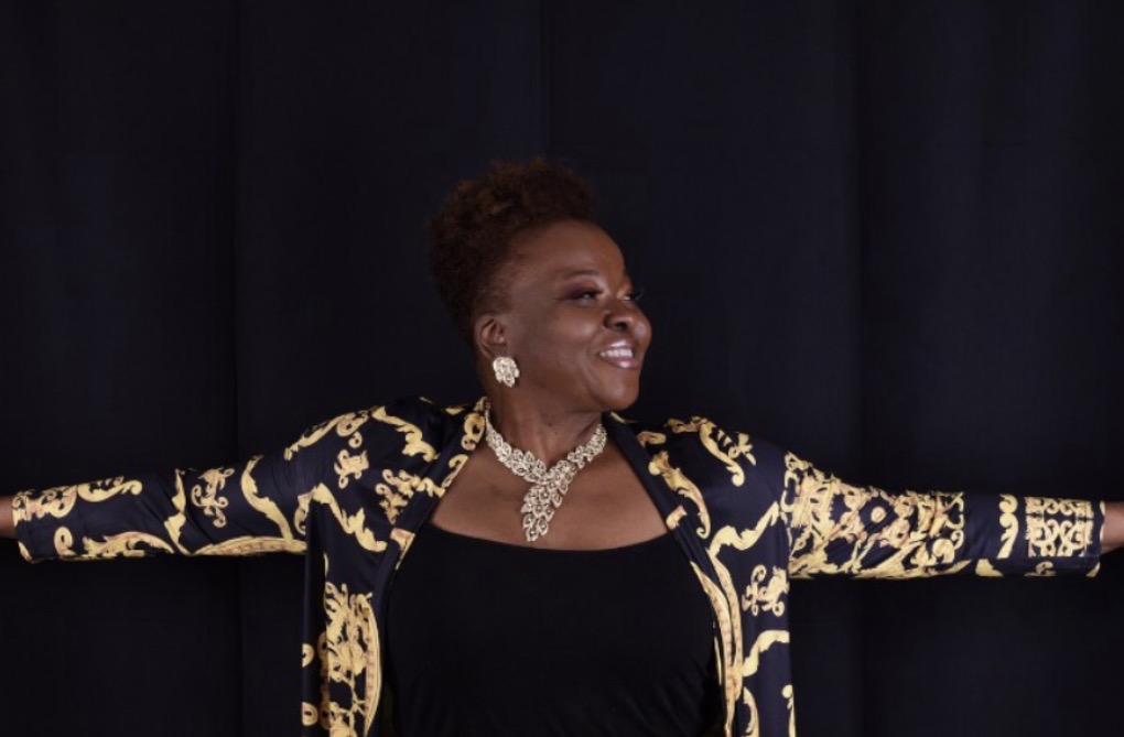 DeeDee Johnson glowing and laughing in a gold and black baroque-print jacket with statement diamond jewelry